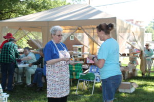 Sister Pat Rhoten talks to Volunteer Doreen Abbott who was helping in the Yard Sale booth. Helping at the money table in the back are Sister Rebecca White (red hat) and Sister Joyce Cecil.
