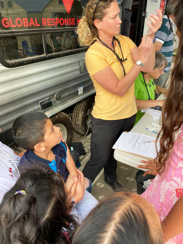 Sister Jacinta Powers, at right in the green shirt, gathers information as one of her fellow volunteers prepares to vaccinate a child with a flu shot.